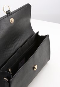 Černá kožená psaníčko otevřené, aby ukázalo hlavní přihrádku se zipovou kapsou a zlatým magnetickým uzávěrem.