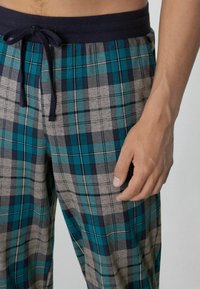 Kostkované pyžamové kalhoty v odstínech tyrkysové, námořnické modři, šedé a bílé. Mají elastický pas se šňůrkou a volný střih. Hladký materiál.