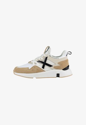 Zapatilla deportiva con malla blanca y gamuza beige, con un diseño de cruz negro, cuello acolchado y suela de goma, con una lengüeta en el talón.