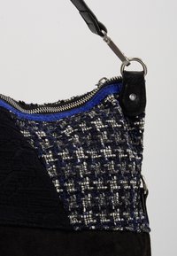 Czarna i granatowa torba z fakturowanej tkaniny z tkanymi wzorami, srebrnym zamkiem błyskawicznym oraz skórzanym paskiem z srebrnymi elementami ozdobnymi.