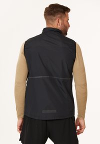 Mustapuku sleeveless-vesti, jossa on korkea kaulus, tekokuitupinta, heijastava raita ja kumimainen logo alhaalla selässä.