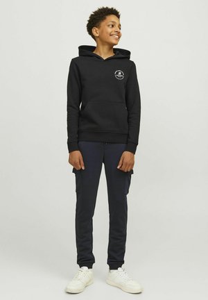 Sweat à capuche noir avec poche frontale, associé à un pantalon cargo bleu marine avec poches latérales, et des baskets blanches avec une semelle texturée.