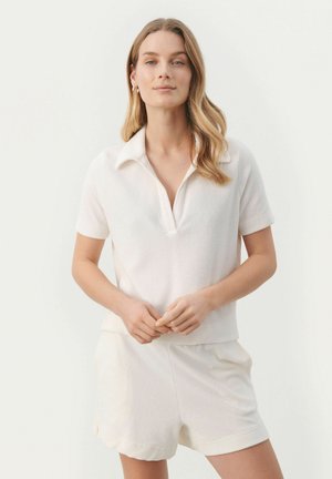 Polo à manches courtes en tissu blanc doux avec un col en V, associé à un short blanc assorti. Design simple et texture lisse.