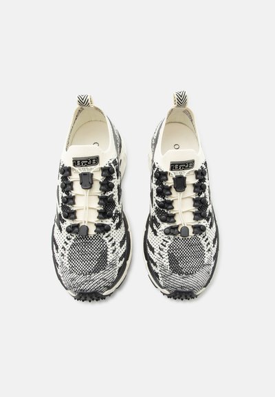 Ζευγάρι ασπρόμαυρα παπούτσια με μοτίβο, ελαστικά κορδόνια χωρίς δέσιμο και θηλιές έλξης, απεικονιζόμενα από ψηλά σε απλό φόντο.