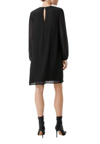 Czarna sukienka z długim rękawem, z dekoltem w kształcie łezki, luźny krój i przezroczyste detale przy rękawach. W połączeniu z czarnymi botkami za kostkę.