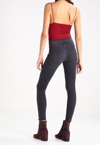 Röd spaghetti axelbandstopp, höga svarta tajta jeans och mönstrade ankelstövlar med mörka blommönster, sett bakifrån.