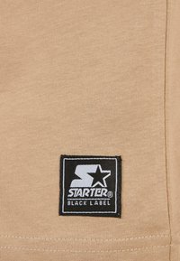 Starter Black Label logó folt világosbézs szöveten, a széleken látható varrással.