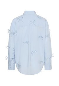 Chemise bleu clair à manches longues ornée de plusieurs petits nœuds décoratifs cousus sur le dos et les manches, sur fond blanc.