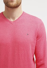 Maglione rosa a scollo a V realizzato in morbido tessuto lavorato a maglia, con un piccolo logo ricamato sul lato sinistro del petto e dettagli delle maniche a coste.