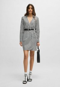 Zwart-wit gestreepte jurk met een V-hals, lange mouwen en een ceintuur rond de taille. Heeft contrasterende manchetjes en is gecombineerd met zwarte accessoires.