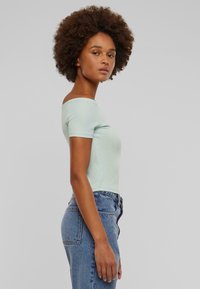 Lyseblå av-og-skulderen topp laget av mykt stoff, med korte ermer og en tettsittende silhuett, paret med høytlivet denimjeans.