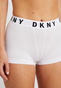 Bijele pamučne bokserice s crnim DKNY logom na pojasu, s glatkom teksturom i uskim dizajnom bez vidljivih šavova.