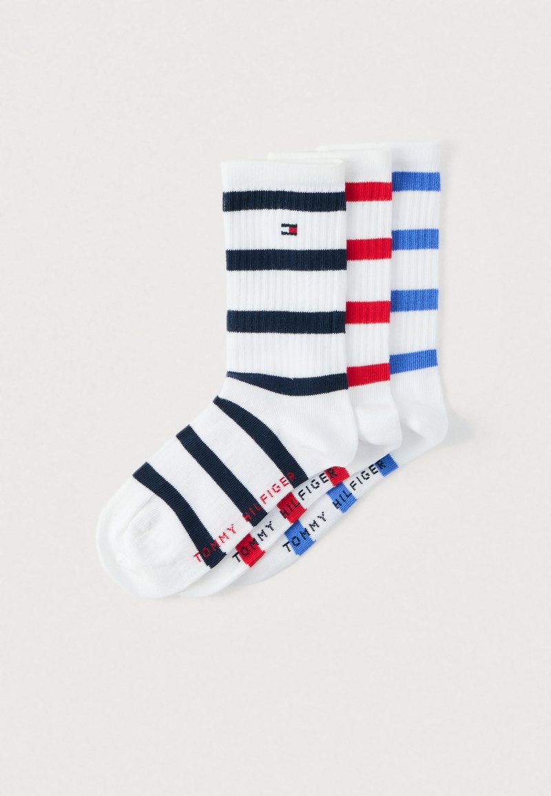 Trzy pary białych skarpetek za kostkę z poziomymi paskami w kolorach granatowym, czerwonym i niebieskim, każda z brandingiem Tommy Hilfiger.
