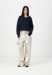 Granatowy, dziergany, krótki sweter z teksturowanym wzorem diamentowym, w połączeniu z błyszczącymi, srebrnymi spodniami typu wide-leg. Dodatki obejmują małą torebkę.