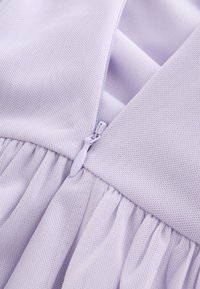 Gros plan d'un tissu violet clair avec motif texturé et une fermeture éclair assortie à une couture entre deux sections froncées.
