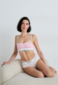Svijetložuti bralette s bijelom trakom koja nosi logo "Calvin Klein", uparen s bijelim hipster gaćicama. Glatka tkanina, bešavna izrada.