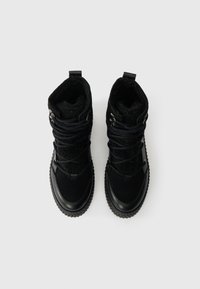 Pár černých zimních bot s tlustými gumovými podrážkami, fleecovou podšívkou a křížovými tkaničkami, pohled shora na bílém pozadí.