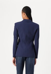 Marineblauer taillierter Blazer mit strukturierten Schultern, maßgeschneiderten Nähten und klassischem Kragen. Kombiniert mit locker sitzenden Jeanshosen.