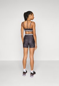 Black sports bra with thin straps and white accents, paired with black patterned shorts. Model wearing black and pink athletic shoes.