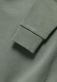 Tejido de algodón verde con un puño acanalado. Textura suave y color uniforme, destacando un diseño simple y minimalista.