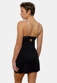 Robe nuisette en satin noir avec bordure en dentelle, bretelles nude ajustables et un détail de dos en trou de serrure. Texture lisse, ourlet évasé.