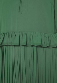Vestido verde con una textura fluida, una cinturilla con volantes y un fondo plisado. La tela parece ligera y suave.