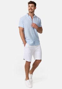 Camicia a maniche corte a strisce blu chiaro e bianche, con bottoni, abbinata a pantaloni corti bianchi con accentuazioni nere, indossata con sneaker bianche.