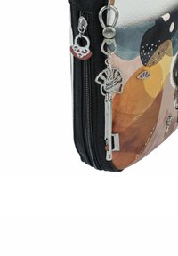 Mehrfarbige Ledertasche mit abstrakten Mustern, einem schwarzen Reißverschluss, silbernem Zubehör und dekorativen Anhängern, darunter ein Baum und ein Schlüssel.