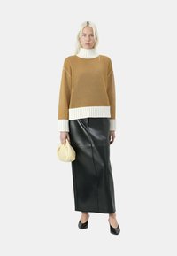 Maglione a maglia senape con colletto alto bianco e orlo a coste, abbinato a una gonna maxi in ecopelle nera e una piccola borsa gialla.