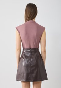 Top ajustado de color rosa claro con mangas corta, combinado con una minifalda de cuero marrón oscuro de cintura alta con cierre de cremallera en la parte posterior.
