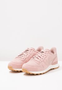 Růžové semišové sportovní boty s texturovaným svrchem, šněrováním a gumovou podrážkou. Obsahují světlé akcenty a polstrovanou podrážku.