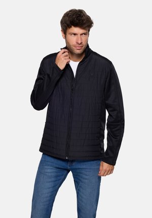 Chaqueta negra con textura acolchada, cuello alto, cremallera frontal y mangas lisas. Combina con vaqueros azules.