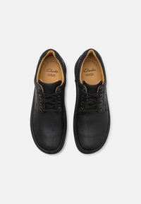 Black leather shoes with round toes, textured finish, lace-up design, and tan insoles featuring "Clarks" branding.