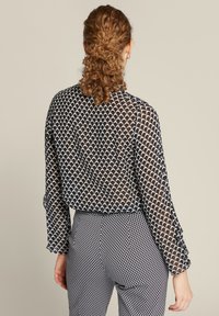 Schwarz-weiße Bluse aus transparentem, strukturiertem Stoff, mit einem Wellenmuster und langen Ärmeln mit Rüschenmanschetten.