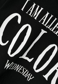 Svart stoff med fet hvit tekst: "JEG ER ALLER FARGE ONSDAG." Teksten har en variert skrifttype. Teksturen ser jevn og glatt ut.