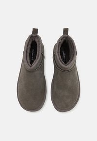 Paire de chaussons gris en suède à enfiler avec doublure en polaire douce et languettes, vus de dessus sur un fond uni.