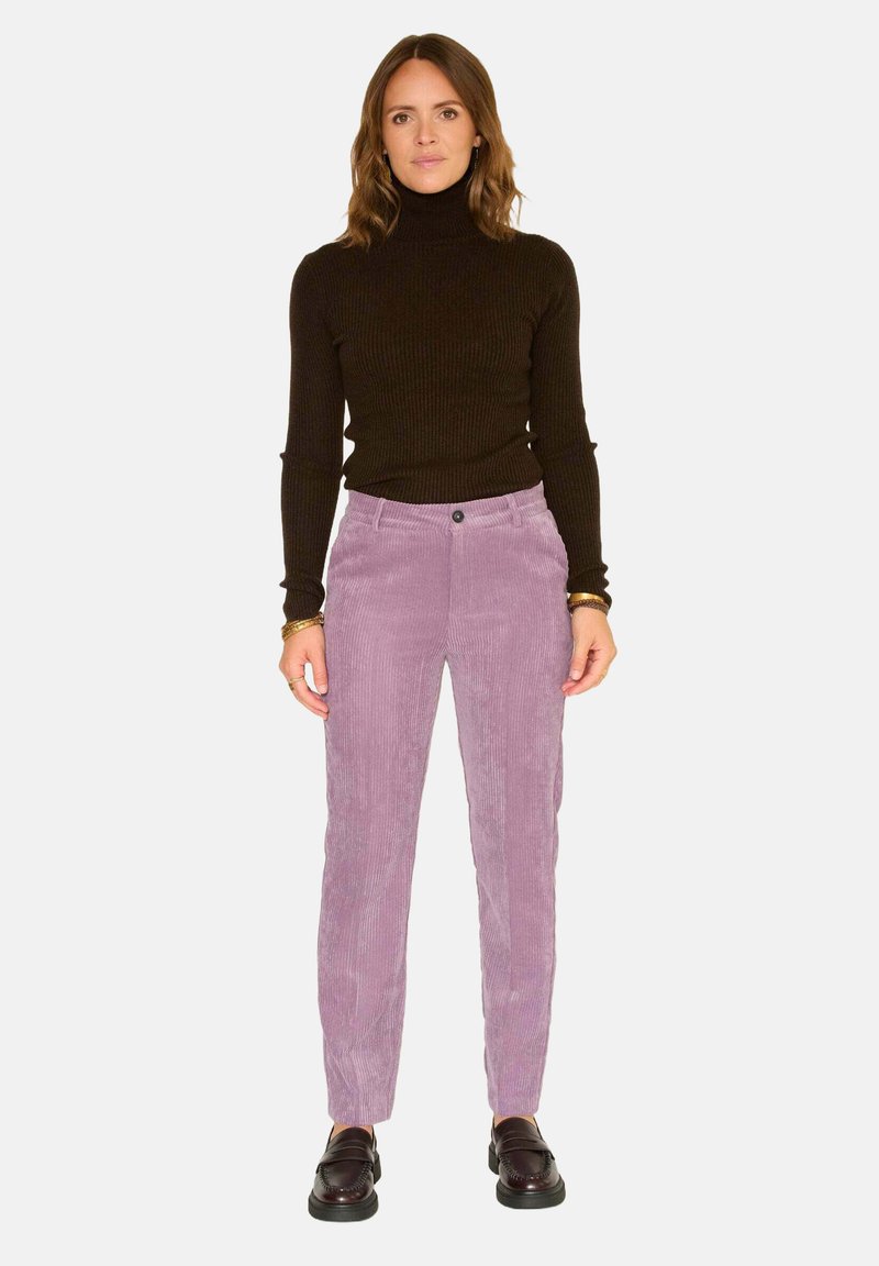 Pantalons en velours côtelé violet avec une coupe droite et une texture à côtes verticales ; associés à un col roulé noir à côtes et des chaussures noires.