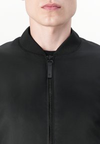Zwarte bomberjack met een gladde textuur, rits aan de voorkant en een geribde kraag. Heeft een minimalistisch ontwerp en geen zichtbare patronen.