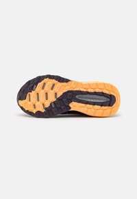 Černá a oranžová podrážka sportovní obuvi s texturovaným vzorem a hlubokými drážkami, navržená pro trakci a stabilitu při venkovních aktivitách.