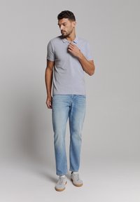 Grijze poloshirt met een kraag, gecombineerd met lichtblauwe jeans en grijze sneakers. De stof lijkt glad met een casual pasvorm.