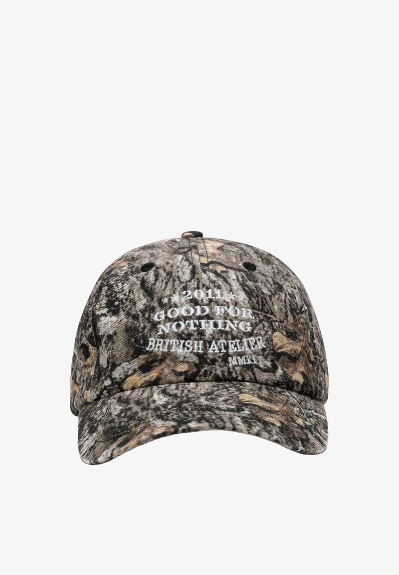 Baseballpet met camouflagepatroon en witte geborduurde tekst aan de voorkant die "2011 Good For Nothing British Atelier MMXI" aangeeft.