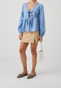 Ljust blå randig blus med djup V-ringning och knytdetalj, kombinerad med en beige minikjol med sidodragning och olivgröna lägenheter.