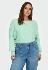 Mintunvihreä, ribbineulottu neule leveällä pääntiellä ja väljälinhkaisilla hihoilla, yhdistetty vaaleansinisiin, korkeavyötäröisiin farkkuihin, joissa sivutaskut.