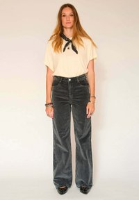 T-shirt oversize jaune clair à manches courtes, associé à un pantalon en velours côtelé noir à taille haute et à jambes larges. Talons hauts noirs cloutés.