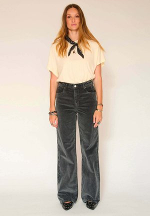 T-shirt oversize jaune clair à manches courtes, associé à un pantalon en velours côtelé noir à taille haute et à jambes larges. Talons hauts noirs cloutés.