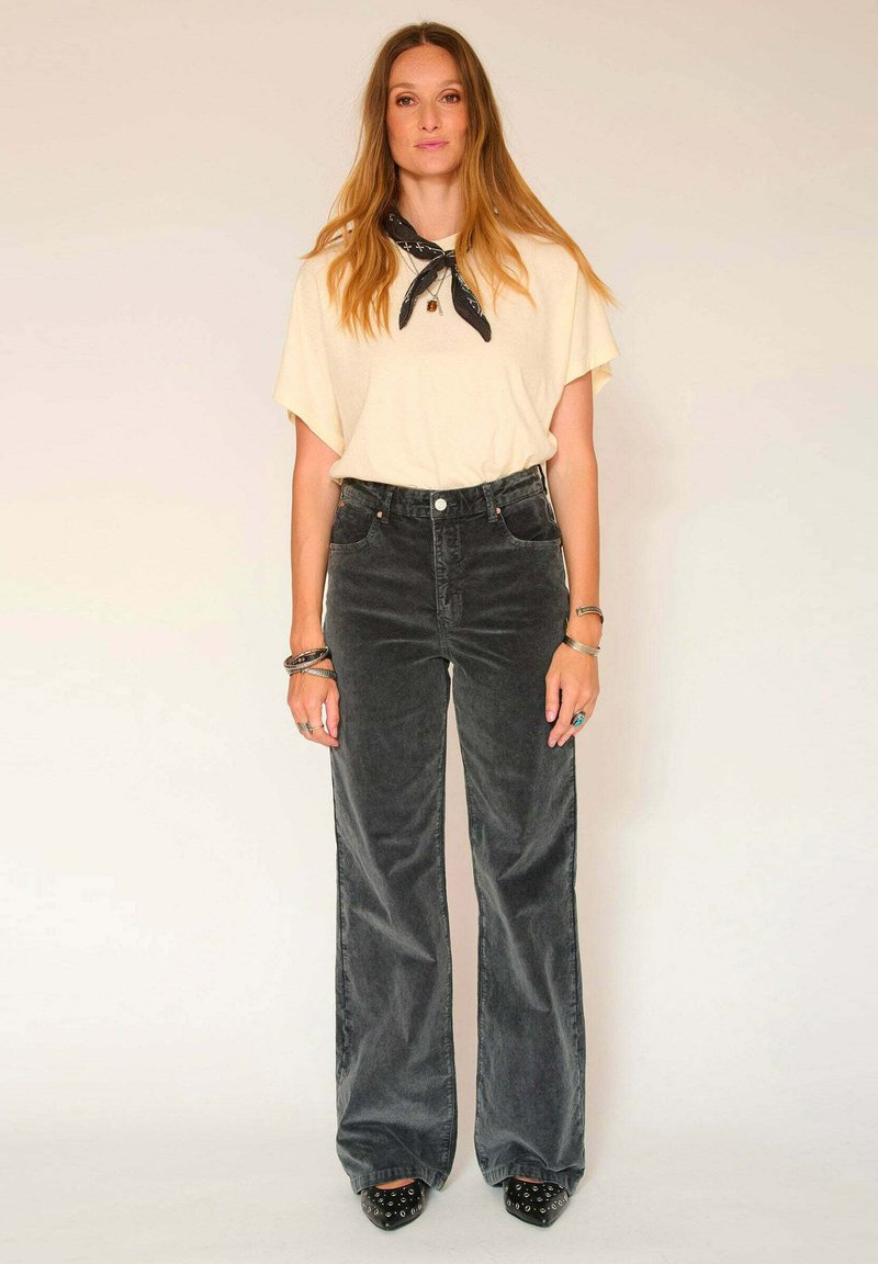 T-shirt oversize jaune clair à manches courtes, associé à un pantalon en velours côtelé noir à taille haute et à jambes larges. Talons hauts noirs cloutés.