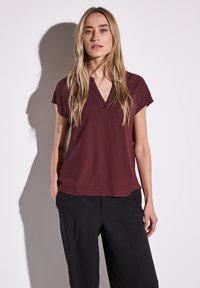 Blusa corta bordeaux a maniche corte con scollatura a V, realizzata in un tessuto morbido, abbinata a pantaloni neri. Design semplice e pulito.