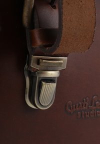 Cintura in pelle marrone con fibbia in ottone, caratterizzata da un fermaglio metallico testurizzato. "Gusti Leathers studio" impresso sullo sfondo in pelle.