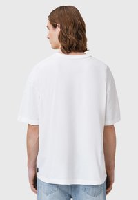 T-shirt bianco a maniche corte realizzato in cotone, con una vestibilità rilassata e un collo rotondo. Il retro mostra un logo discreto all'orlo.