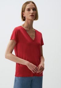 Rode T-shirt met korte mouwen en een V-hals ontwerp. Zachte, gladde stof, aangesloten vorm en een licht gebogen zoom. Minimale naden en details.